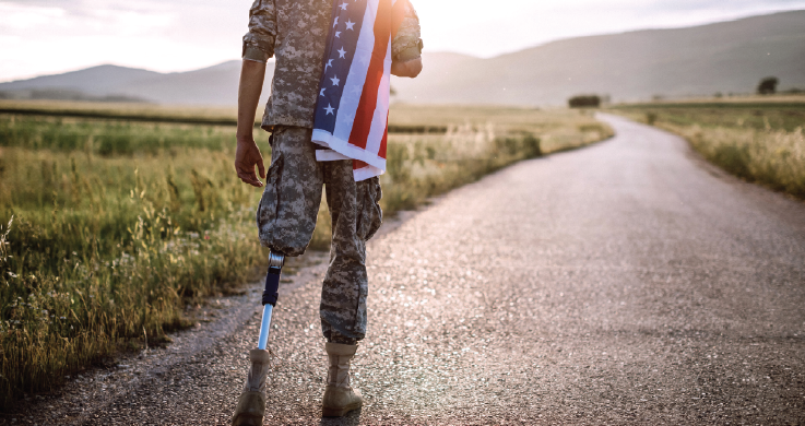 Disabled veteran walks towards sunset holding an American flag